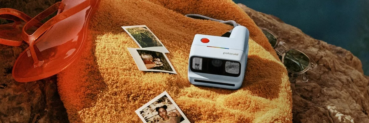 Polaroid Go (Gen 3) položený na ručníku u vody vedle instantních fotografií a slunečních brýlí.
